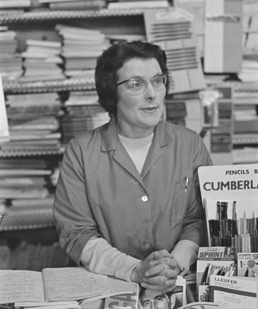 Arianwen Parri stands behind a counter in the shop surrounded by notebooks, pens, and office supplies.